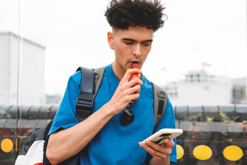 Young man using vape while checking smartphone in  urban setting