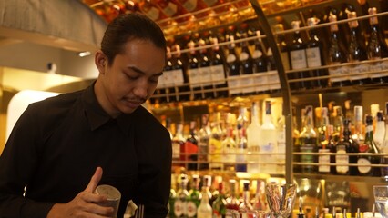 Smiling Asian smart bartender shaking with two hands in mixed cocktail in shaker preparing at luxurious counter bar, preparation special refreshment alcohol drink nightlife warm nightclub. Vinosity.