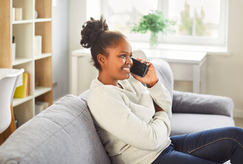 Young african american woman talking on phone at home, happy girl holding cellphone making,...