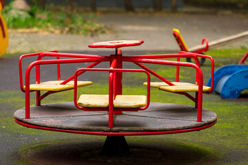 A weathered red merry-go-round sits alone in a deserted playground, hinting at childhood memories...