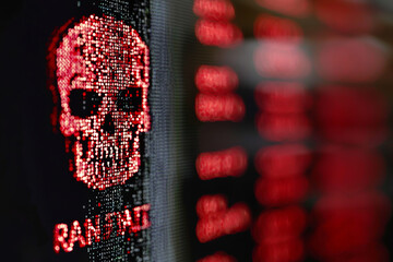 dramatic close up of computer monitor displaying red skull symbol, representing danger and cyber threats. background features blurred text, enhancing ominous atmosphere