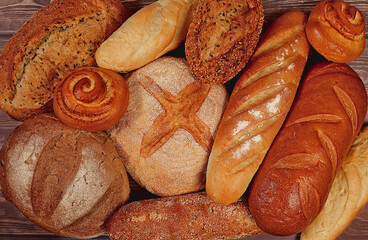 Freshly baked bakery products, whole grain homemade bread, different types of round sourdough bread with crispy crust, baguettes, buns and ears of wheat on wooden background, modern baking concept,
