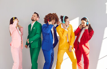 Group of happy people in colorful business suits dancing to music, wearing headphones, against a...