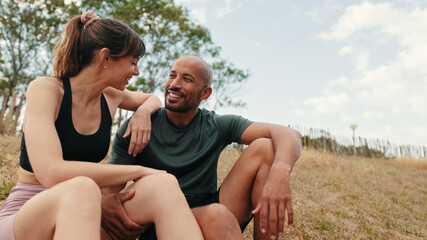 Side view of multi-ethnic male and female athletes sitting on a hill under trees, hugging, talking and supporting each other. Training together and couple goals. Motivation and dreams