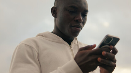 Close-up of a fit guy smiling while using mobile phone and chating outdoors, scrolling social networks