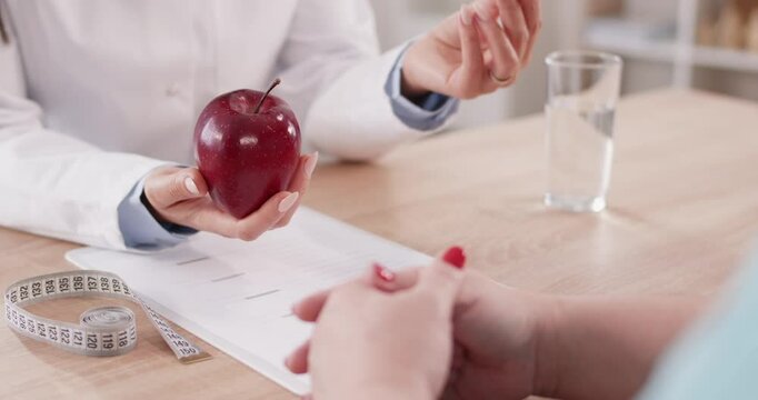 Close up view of a hands of a nutritionist, holding an apple while providing detailed advice and formulating a personalized diet plan during a focused and informative consultation with the patient.