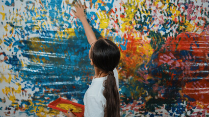 Young happy girl holding the color tray and paint colorful stained wall to express idea and enhance imagination with hand print. Caucasian girl stamp hand to decorate room in art lesson. Edification.