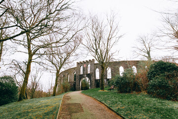 McCaig's Tower in Oban, Scotland - Historic Stone Structure with Arched Windows and Battlements, Surrounded by Bare Trees, Greenery, and a Winding Path in a Peaceful Park