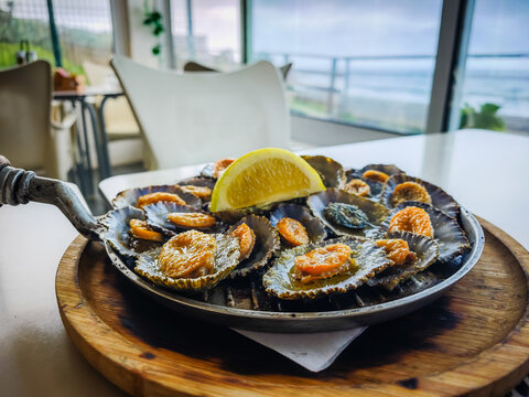 Grilled limpets served on a cast iron with a lemon slices in a restaurant in Azores island. Typical Atlantic ocean region seafood dish
