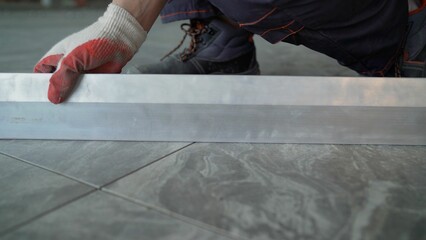 Professional contractor carefully installing precision aluminum threshold on sleek grey ceramic...