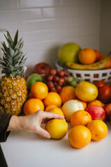 Woman's hand selecting fresh citrus fruit from a colorful kitchen assortment with modern backsplash 