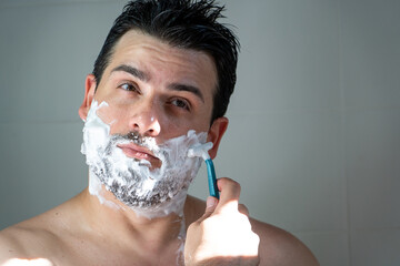 Hombre apuesto afeitándose la barba usando espuma