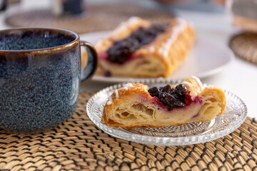 A slice of pie with berry filling on a glass plate and a mug of coffee on a dining table. Photo