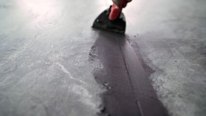 Construction professional carefully spreading dark sealant along concrete expansion joint using...