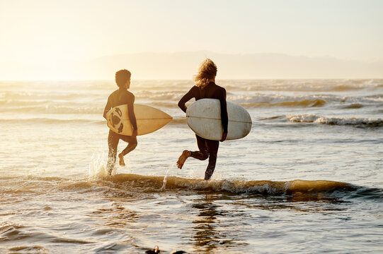 Surfing, friends and running at sunset beach for waves, freedom and swim on travel from behind. Surfboard, surfer and guys at sea, ocean and excited adventure on holiday, summer and fun water sports