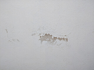 Damaged white wall texture close-up with peeling paint and exposed plaster. Textured surface, irregular damage patterns, effects of wear, moisture, deterioration, aging on interior and exterior walls.