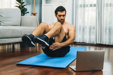 Obraz premium Athletic and sporty man doing crunch on fitness mat while follow online home workout exercise instruction for fit physique and healthy sport lifestyle at home. Online gaiety home exercise video.