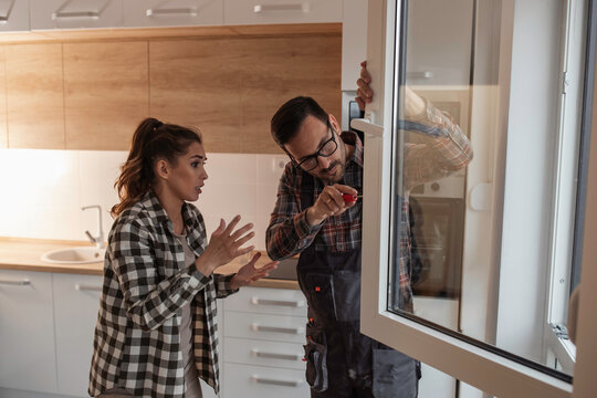 Worker fixing window beside woman in apartment