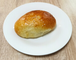Freshly baked bread roll with sesame seeds on a white plate set against a light wooden background