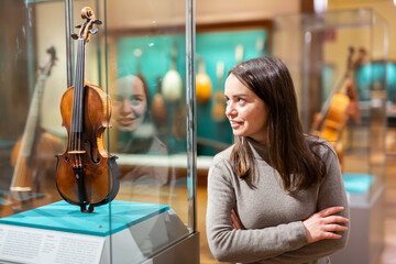 Portrait of interested adult brunette visiting exhibition of medieval musical instruments in...
