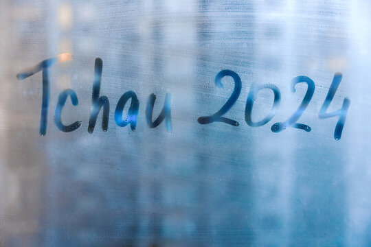 lettering Tchau in Portuguese language is bye in English and numbers 2024 is twenty twenty-four paint on foggy blue glass of window in city