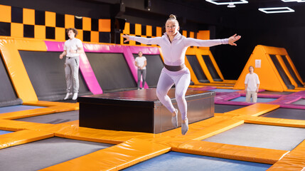 Active adult woman trains jumping on trampoline in trampoline center
