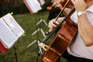 cellist performs in an outdoor classical music ensemble, with sheet music on stands and other...