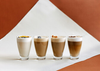 A selection of four crafted coffee beverages, each topped with unique garnishes, arranged against a stylish brown and white backdrop.