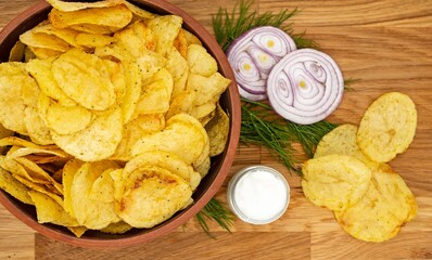 Crispy chips with onions and sour cream on a wooden board.
