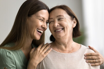 Close up portrait two beautiful different generation women, daughter and mother smiling warmly looking at each other with love and tenderness, hugging indoor. Happy family, ties, bond, understanding