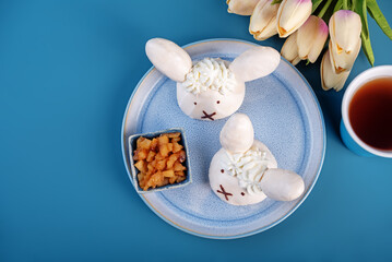 Meringue cake with apple filling and whipped cream on top in the form of funny rabbits in a plate