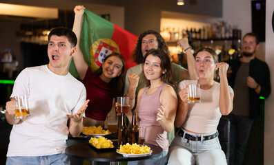 Group of friends fans watching match cheering with Portugal flag in bar