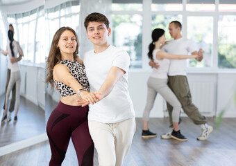 Couple of smiling young guy and girl enjoying slow foxtrot in dance studio. Amateur ballroom dancing concept..