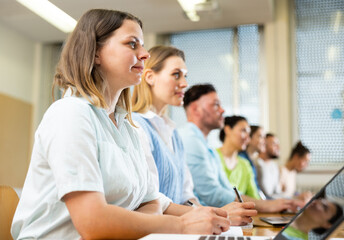 Portrait of a young girl student studying on a laptop and writing synopsis in a copybook during classes in a university ..auditorium with fellow students
