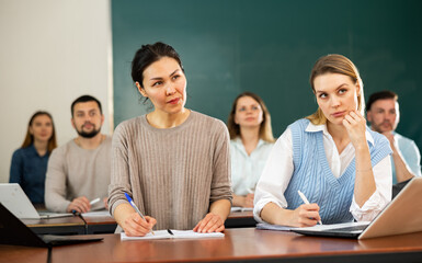 Asian and caucasian women university students sitting at table during lesson.