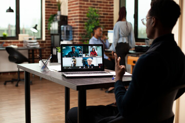 Black entrepreneur attending virtual training with colleagues, discussing business ideas at desk. Male manager seated in office, presenting startup project plans during video meeting with clients.