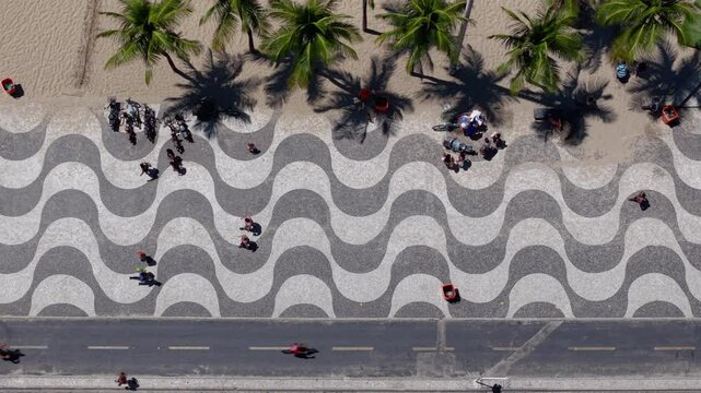 Aerial directly above Copacabana Beach boardwalk with people and palm trees, Rio de Janeiro. Slow motion