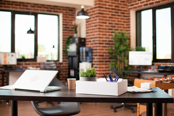 Spacious startup office features clean desk with laptop and business materials, providing modern setup for workers. Well organized brick wall workplace is ready for next project or company research.