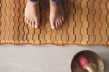 Yoga woman legs standing on nails with singing meditation bowl top view closeup