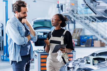 African american serviceman in car service uses tablet to show client invoice after repairing fuel...
