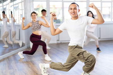 Fototapeta premium Positive woman and man engaged in dancing in group practices energetic swing in a dance studio