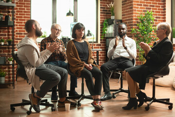 Supportive community clapping for young woman during aa meeting in brick wall office. Caucasian lady sitting in middle of circle being celebrated for mental health recovery at group therapy session.