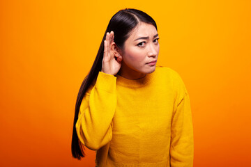 Woman with her hand over ear, trying to listen closely to something, exuding curiosity and...