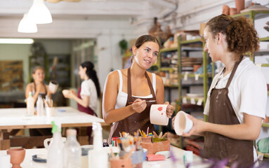 During master class, male participant draws pattern on walls of white ceramic bowl with brush. Girl paints blank, makes individual order. Hand made art, creative pastime.