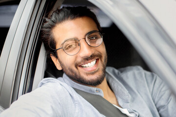 Cheerful indian man driving car, shot from outside, going on trip during summer vacation, side...