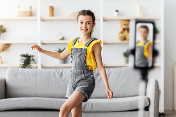 Gen Z Entertainment. Full body length of positive adolescent girl dancing filming video for social network using cell phone camera, creating trendy content for likes with gadget on tripod stabilizer