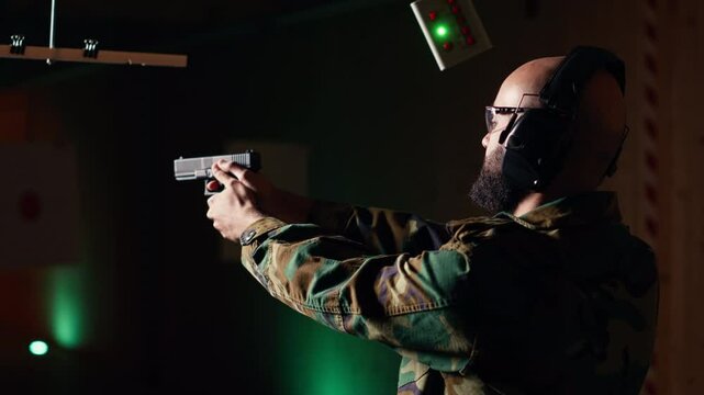 Portrait of happy man training in shooting range, learning pistol holding etiquette, engaging targets at extended range. Joyous army soldier firing lethal fire weapon, camera B