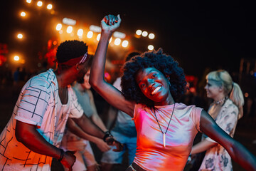 Young woman dancing and enjoying music festival with friends at night