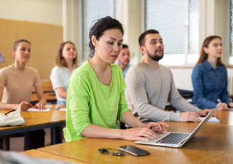 Portrait of female student writing lectures in workbooks and laptop in classroom during lesson