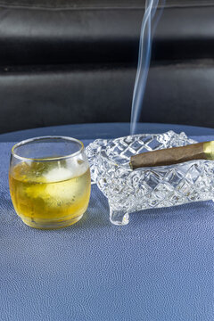 Smoking cigar in a crystal ash tray next to a glass of whisky